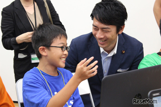 Minecraftコースの中学2年生から、Minecraftについて説明を受ける小泉氏。明瞭な回答と解説に「説明能力が高いね！」と驚く場面も。何かを作る楽しみや今自分が行っていることを熱心に話すようすに、小泉氏は深い感銘を受けていた